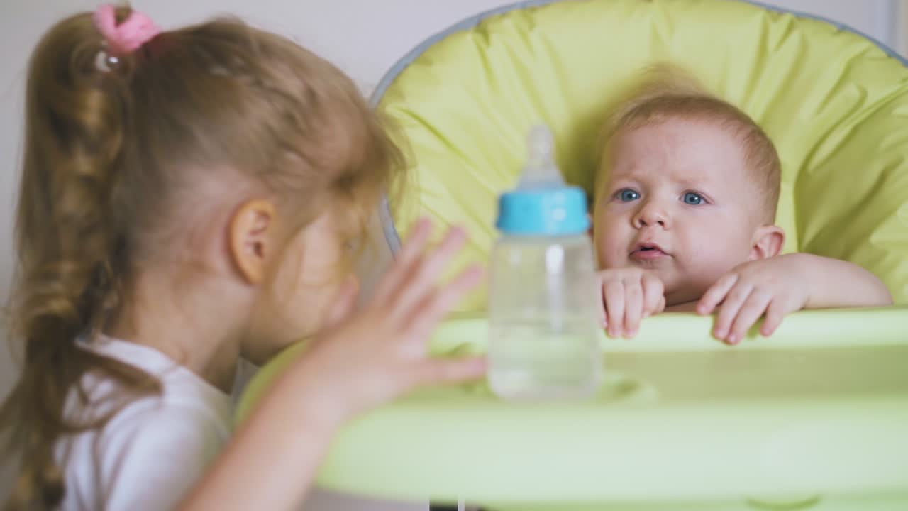 소녀 는 높은 의자 에 앉아 있는 작은 소년 에게 물 병 을 준다