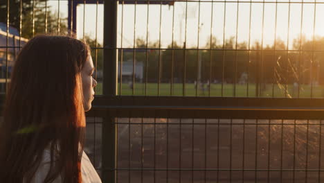 young woman with red hair standing in a field at sunset