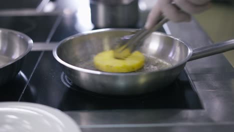 un círculo de piña frito en mantequilla en la sartén en la cocina del restaurante. mano masculina en guante blanco moviendo frutas en utensilios de cocina en cámara lenta. chef irreconocible preparando un plato delicioso.