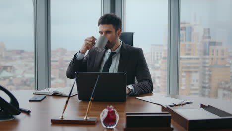 ceo enfocado mirando la pantalla de la computadora portátil bebiendo café en un lugar de trabajo moderno de cerca
