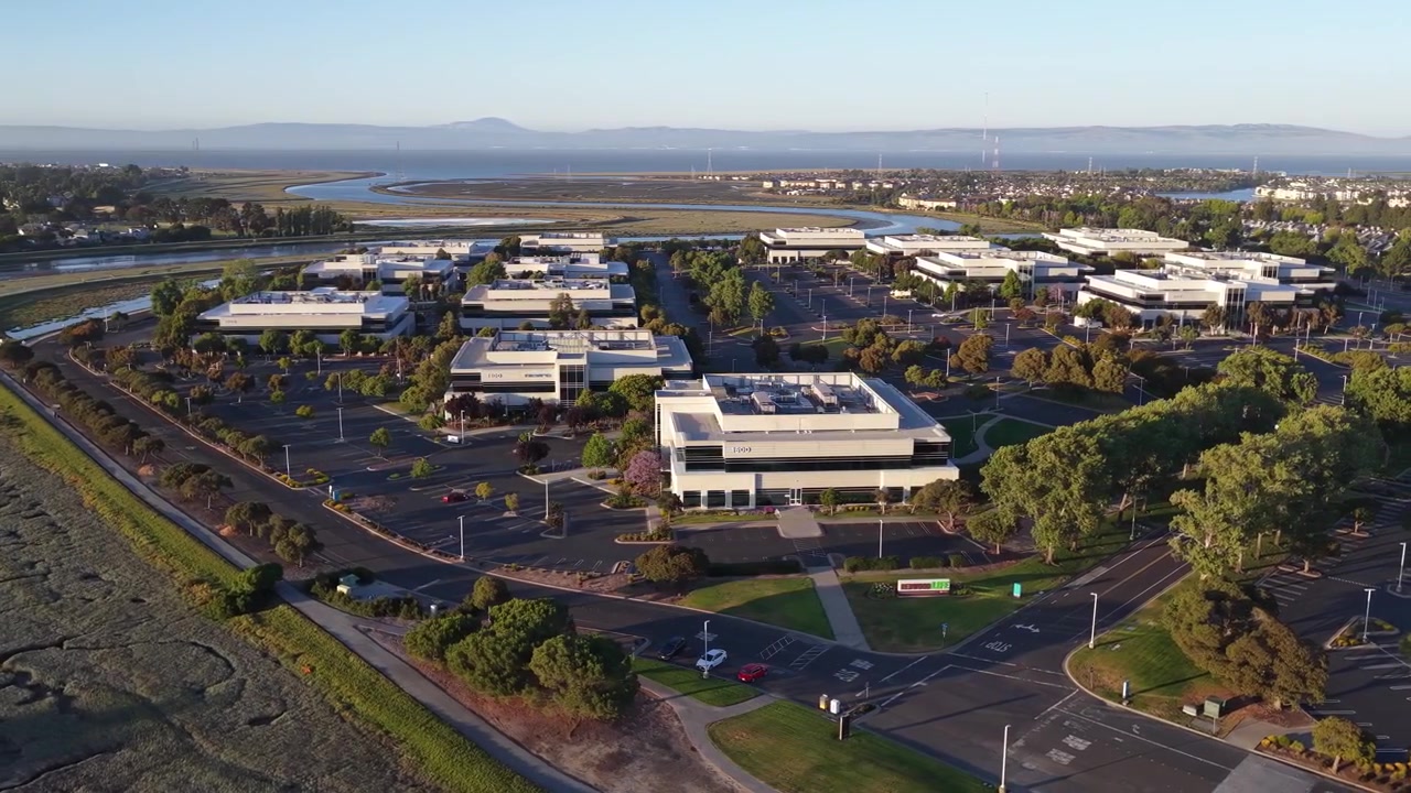 Riprese aeree all'ora d'oro che mostrano i moderni edifici per uffici e gli ampi parcheggi di un parco commerciale situato sulla costa di Redwood Shores, vicino alla Baia di San Francisco in California.