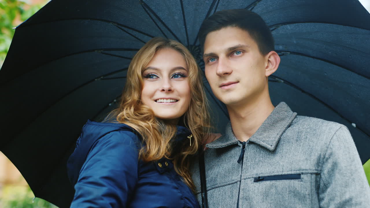 el hombre bien vestido con su esposa de pie bajo un paraguas sonriendo riendo