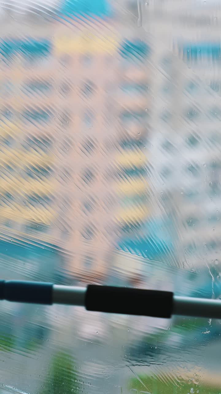 Brush cleaning dirty window with water and soap. Washing glass window inside on city building background. Vertical video