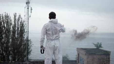 Man-in-protection-suit-standing-on-the-edge-of-the-roof-with-smoke-stick