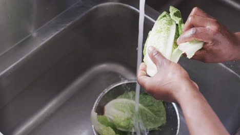 african american male chef washing vegetables in sink in kitchen, slow motion