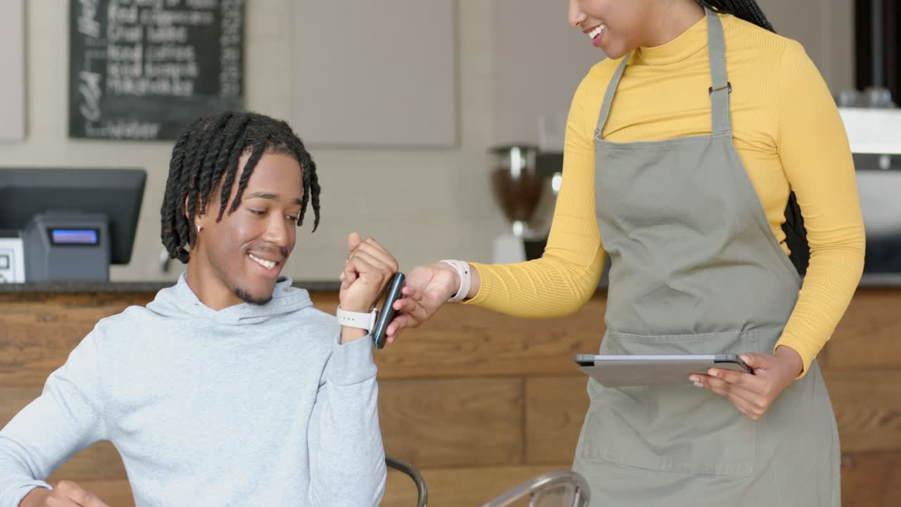 Un uomo afroamericano tocca lo smartwatch mentre il barista gli porge il lettore per completare l'ordine al bar
