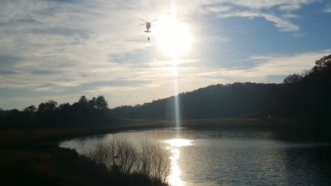 el helicóptero blackhawk de la guardia nacional del ejército obtiene agua con un balde bambi para combatir incendios en las montañas el helicóptero pasa a través del sol mientras desciende para obtener agua
