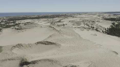 drone shot flying to the left, with 2 people walking over the dunes