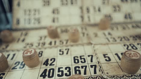 video macro de un tablero de bingo, luces de estudio, 120 fps, cámara lenta, dígitos de chips de madera, imágenes en bruto, juego de mesa de lotería vintage, números de cartas, grúa tirando hacia atrás movimiento suave, disparo de revelación