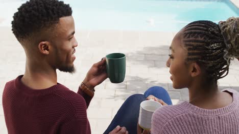 feliz pareja afroamericana abrazándose y relajándose con café fuera de la casa