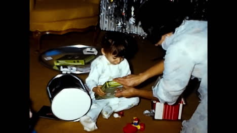 baby sitting on floor, playing with toys. circa usa - 1970s: a baby from a 1970s video archive in the usa sits on the floor, engrossed in playing with various toys.