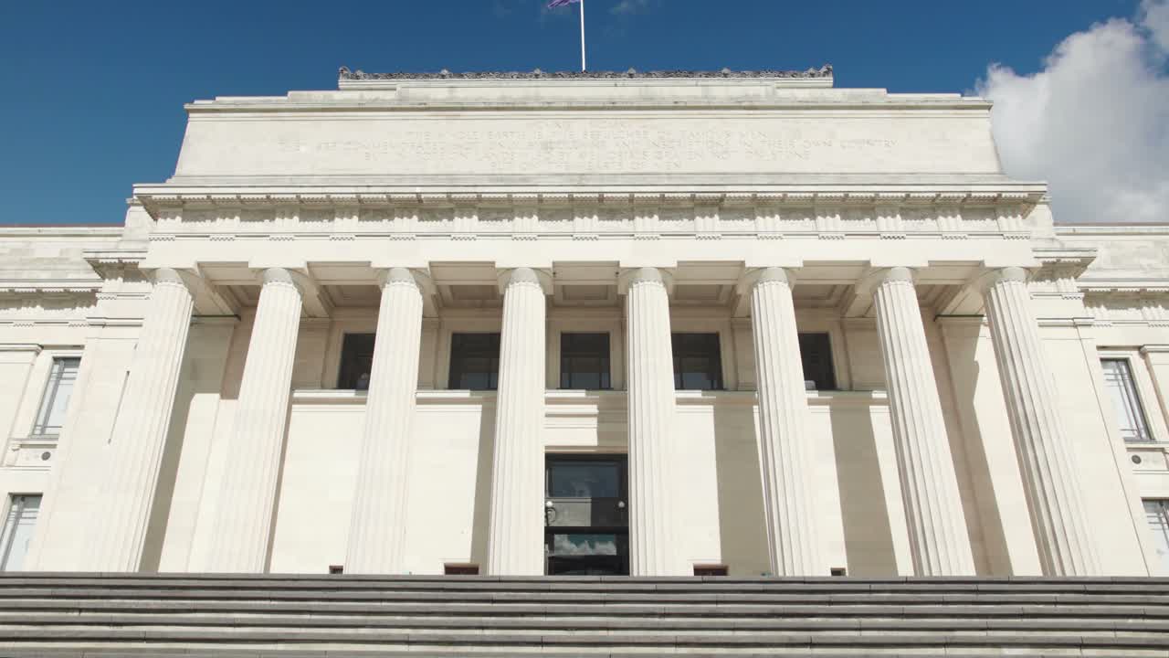 Straight on symmetrical low angle view of the Auckland War Memorial Museum and its staircase on the Auckland Domain with a blue sky and clouds in the background