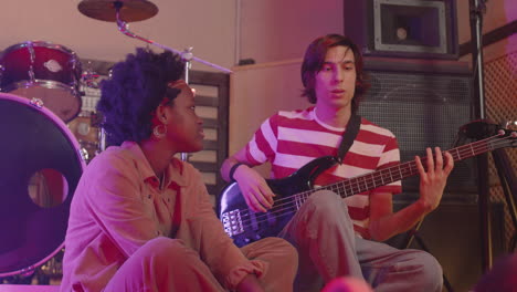 boy playing guitar and girl watching him while rehearsing in recording studio 1