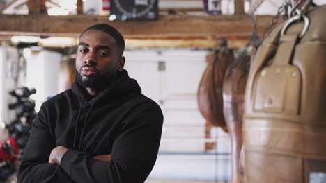 portrait of male boxer in gym standing by old fashioned leather punch bag