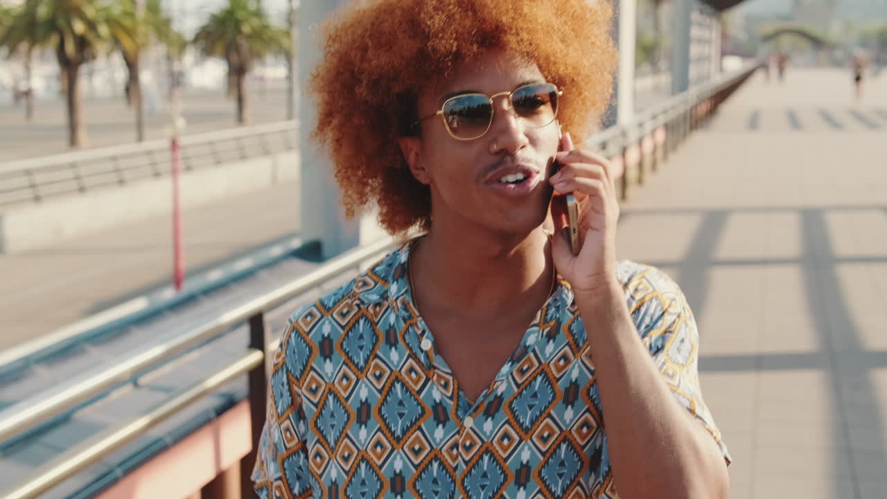 Happy Young Man with Curly Hair Talking on Phone Outdoors