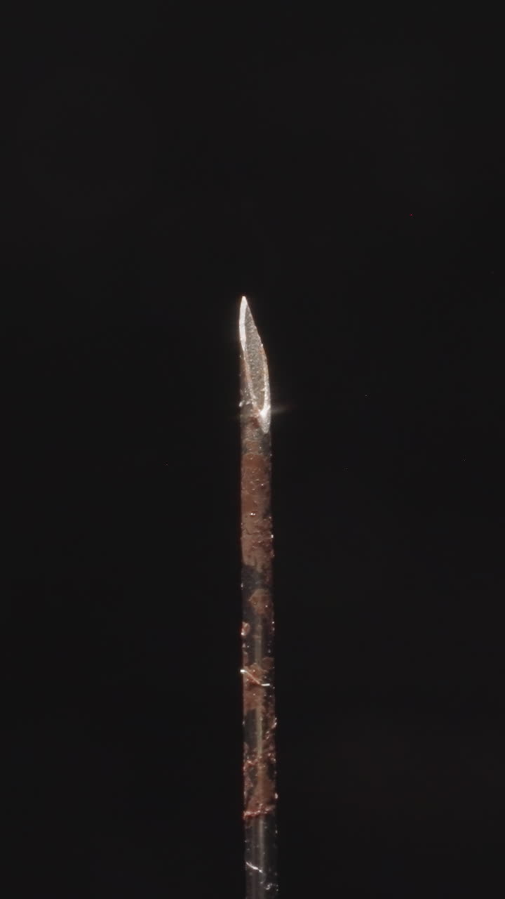 Rusty needle of old medical syringe turning on black background. Hypodermic tool used for injecting substances into body or extracting fluids macro