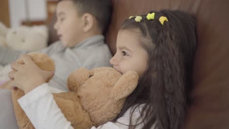 close-up face of a cute middle eastern girl sitting with her brother at the coach and holding teddy bear