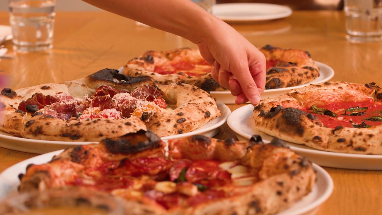 Un cameriere posiziona diverse pizze napoletane fresche su un tavolo di legno con illuminazione calda