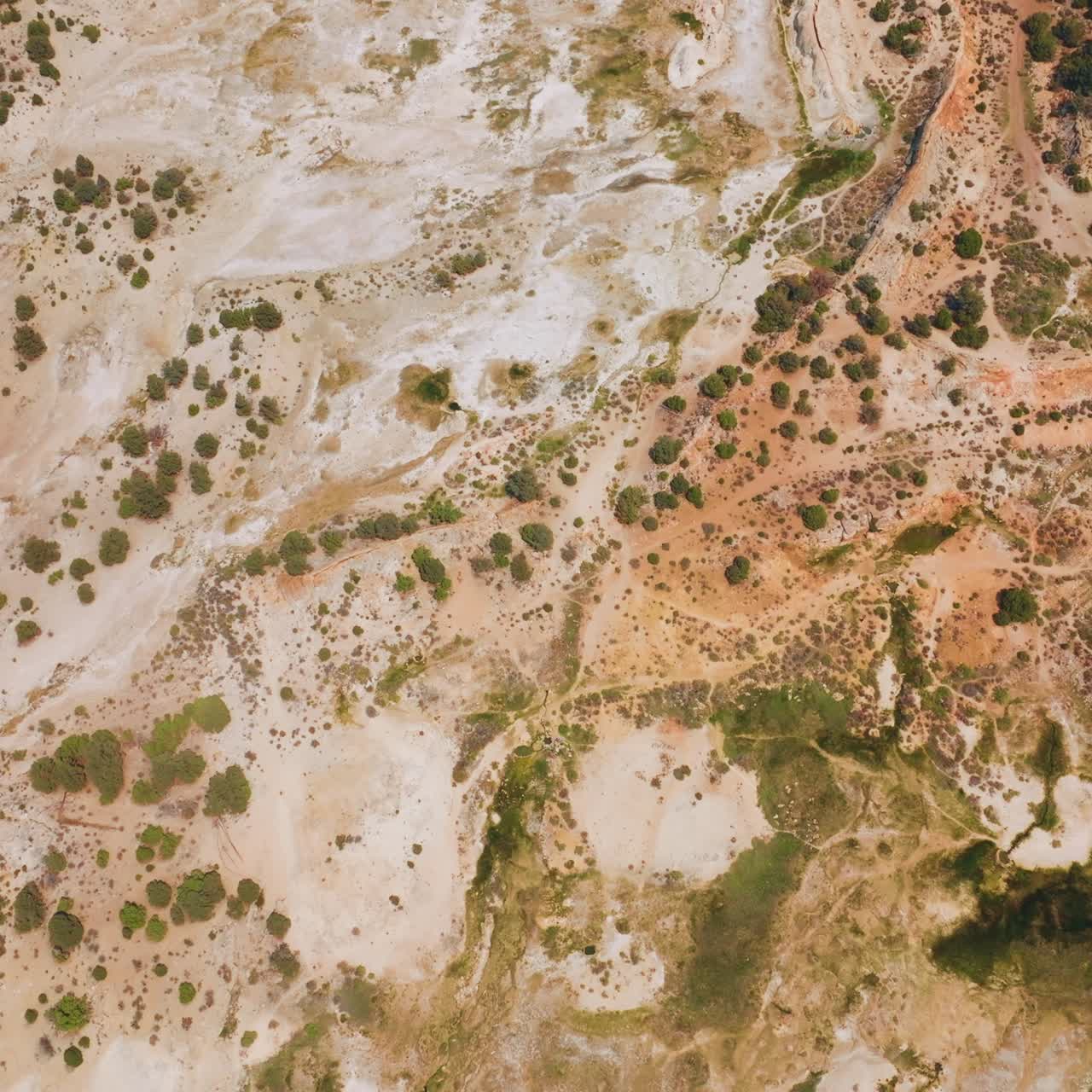 Descending above the rocky landscape with some scarce greenery. Bare dry ground of Travertine Hot Springs from top view
