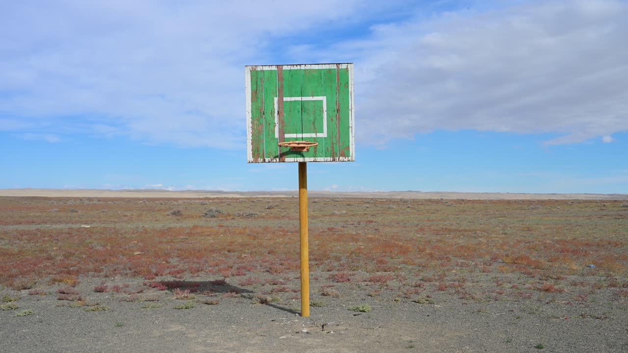 A lone, weathered basketball hoop stands in the middle of a vast and empty landscape, a surreal and unexpected sight in the remote Mongolian steppe