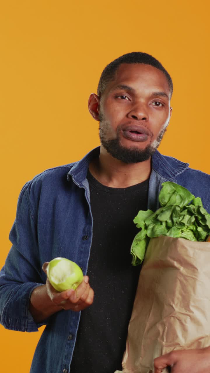 Jovem negro comendo uma maçã verde fresca tirada de uma sacola de compras