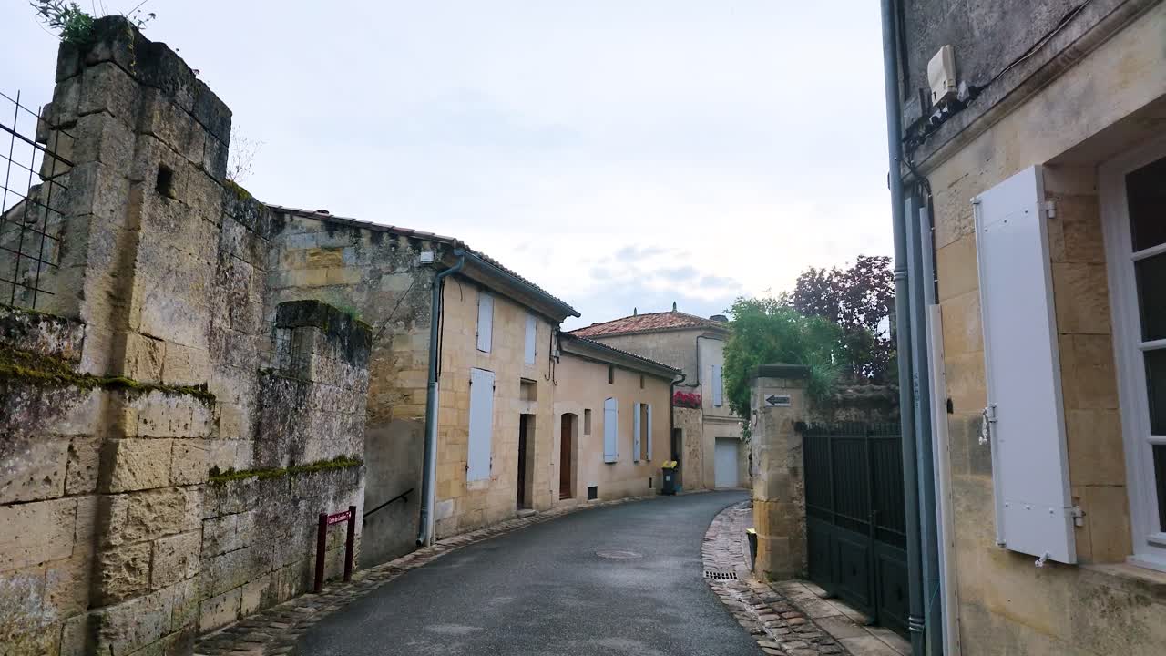 Una lenta panoramica della telecamera cattura antiche mura in pietra calcarea e persiane lungo una tranquilla strada medievale.