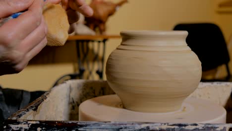 professional potter shaping pot with special tool in pottery workshop