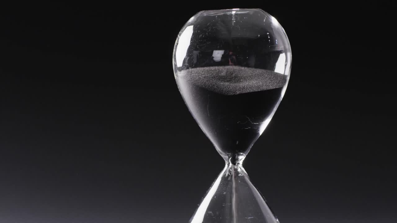 Video of hourglass with sand pouring, copy space on black background