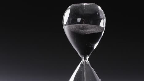 video of hourglass with sand pouring, copy space on black background