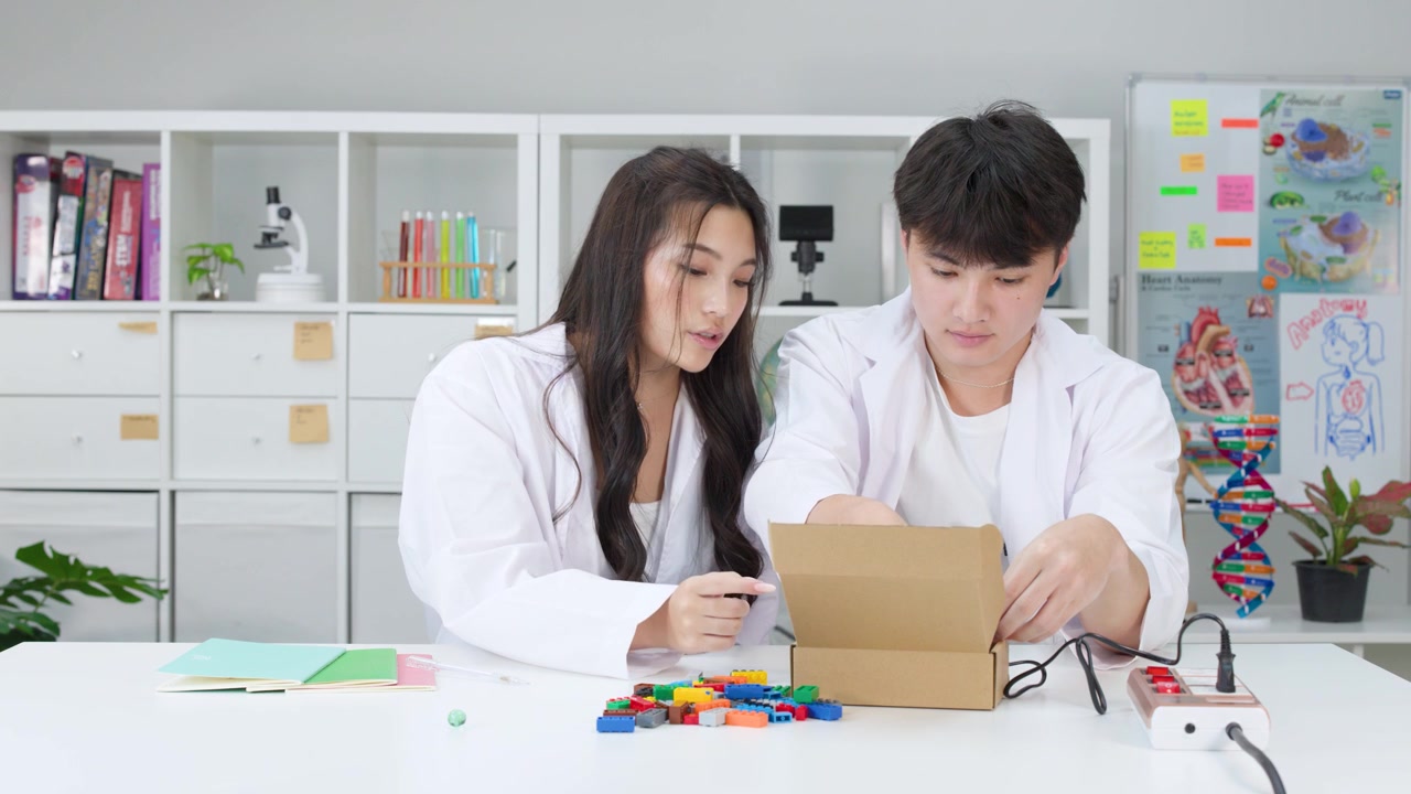 白衣を着た2人の学生が、プラスチック製のブロックと箱を使ってSTEMプロジェクトで協力する