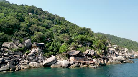 seaside cabins on rocks in mango bay ko tao island thailand by shore, aerial pan left shot