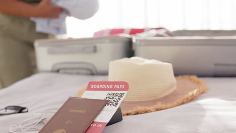 passport and boarding pass in focus on a bed, with a straw hat and sunglasses nearby