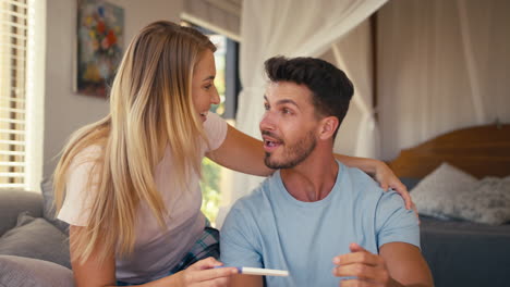 excited couple in bedroom at home celebrating positive pregnancy test result