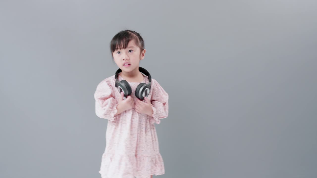 헤드폰을 끼고 있는 귀여운 아시아 소녀는 음악과 춤을 즐기며 스튜디오에서 행복하게 돌아다닙니다
