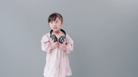 헤드폰을 끼고 있는 귀여운 아시아 소녀는 음악과 춤을 즐기며 스튜디오에서 행복하게 돌아다닙니다
