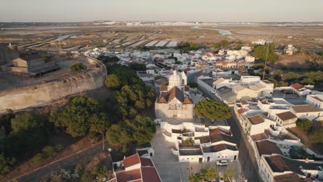 aerial pull out shot reveals the town square of church of our lady of martyrs in castro marim