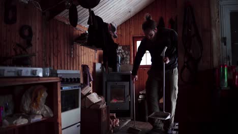 Chico-Adulto-Barriendo-Dentro-De-Una-Cabaña-De-Invierno-De-Madera-Rústica