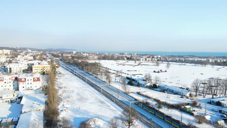 long passenger train driving on a railway track in a winter landscape with buildings covered with white snow on a sunny day in gdansk poland