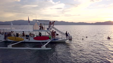 aerial view of a party boat with boat slide and a tourist sliding off into the water during sunset at philippines, palawan.