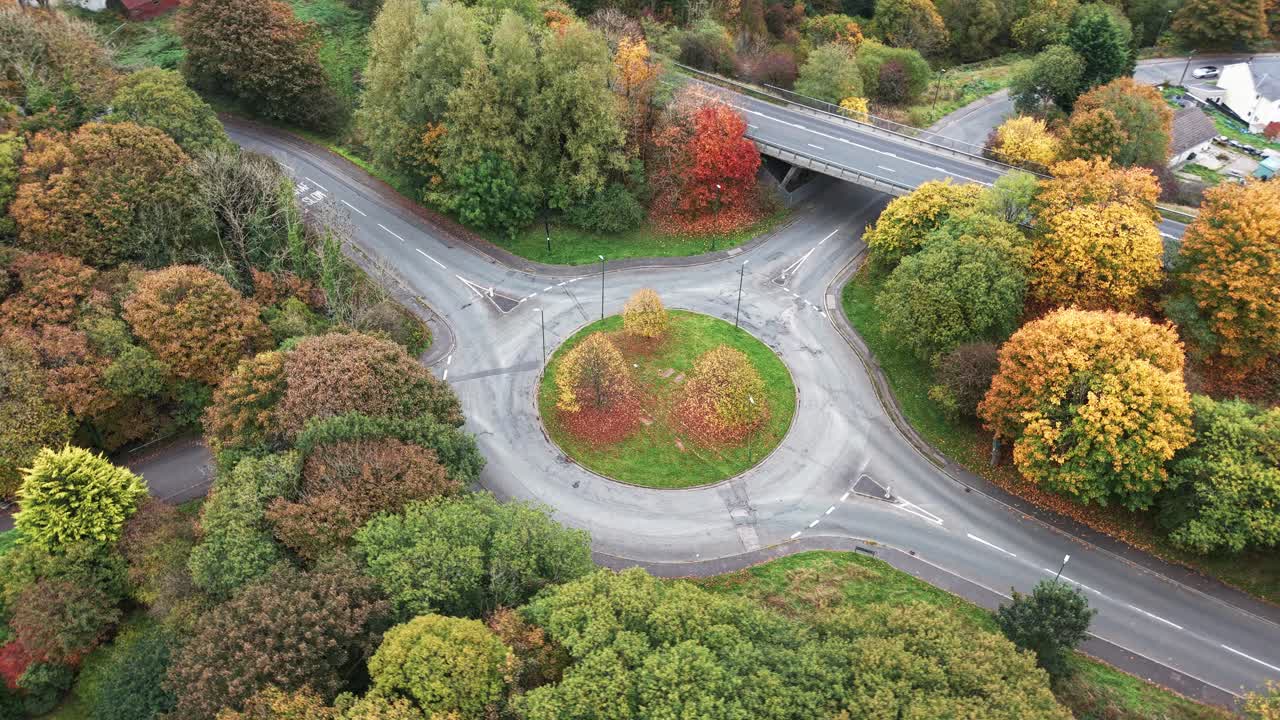 Orbiting drone shot of a quiet traffic roundabout surrounded by trees in autumn colours