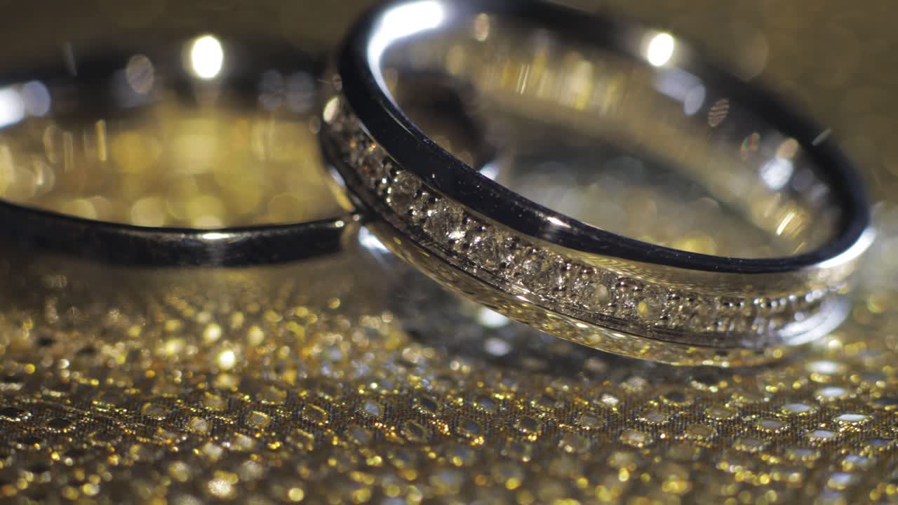 Wedding rings lying, rotate, spinning on shiny golden shining surface with light, close-up macro