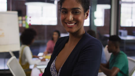 feliz mujer de negocios de raza mixta de pie y sonriendo con colegas en el fondo