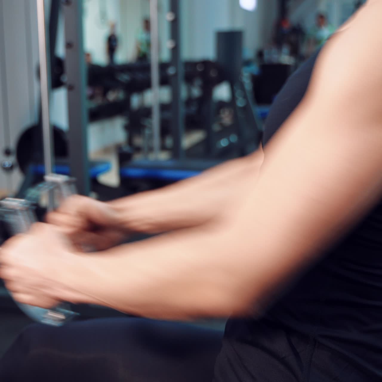 A woman in a black top performs an exercise for pumping the press and biceps against the background of sports equipment in a fitness club. Close-up