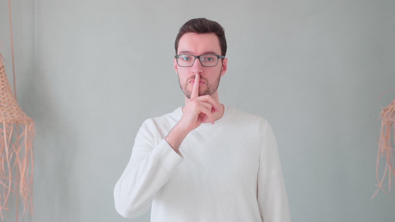 Giovane uomo con il dito davanti alla bocca, segno di calma e segretezza, mantieni il segreto, non dirlo, non fare rumore, stai zitto