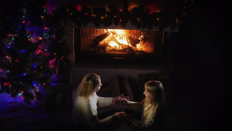 mamá juega con su hija cerca de la chimenea y el árbol de navidad para pasar un buen rato juntos