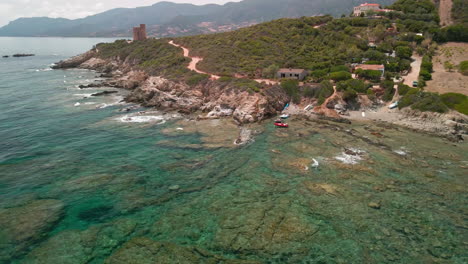 Mediterrane-Landschaft-Mit-Blick-Auf-Das-Meer-Mit-Schlauchbooten,-Die-An-Den-Ufern-Festgemacht-Sind,-Und-Wellen,-Die-Gegen-Die-Felsen-In-Sardinien,-Italien,-Brechen---Statische-Luftaufnahme