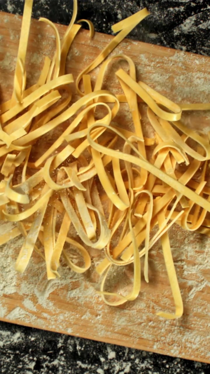 Tagliatelle crude appena fatte con farina su un tagliere di legno