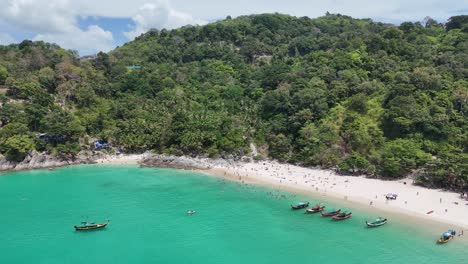 aerial footage of a vibrant, crowded beach in phuket, thailand, showcasing turquoise waters, lush greenery, and anchored longtail boats