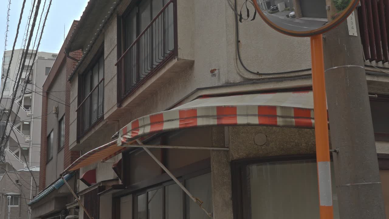 A cozy, older corner building with a distinctive red and white striped awning and classic Japanese residential features, capturing a slice of urban daily life.
