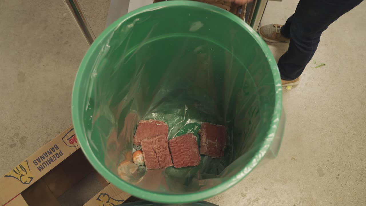 Tossing spoiled meat to be thrown away into bin by chef in kitchen.